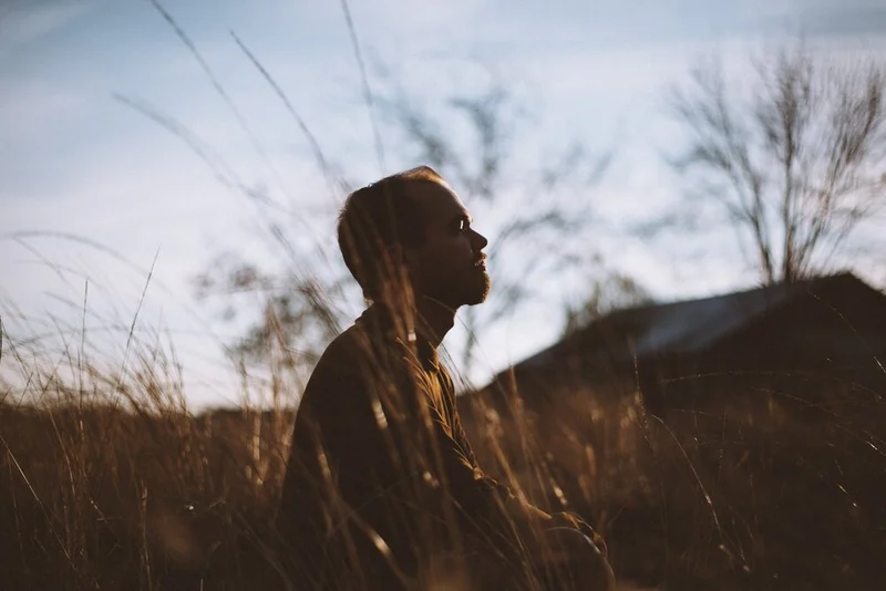 silhouette-of-man-sitting-on-grass-field-at-daytime-775417